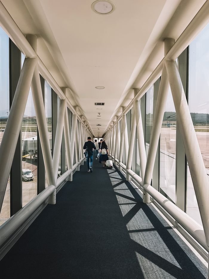People walking in a glass airport corridor with a diminishing perspective.